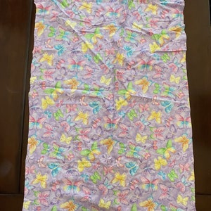 May include: Purple fabric with a repeating pattern of colourful butterflies. The butterflies are in various shades of pink, yellow, green, and blue.