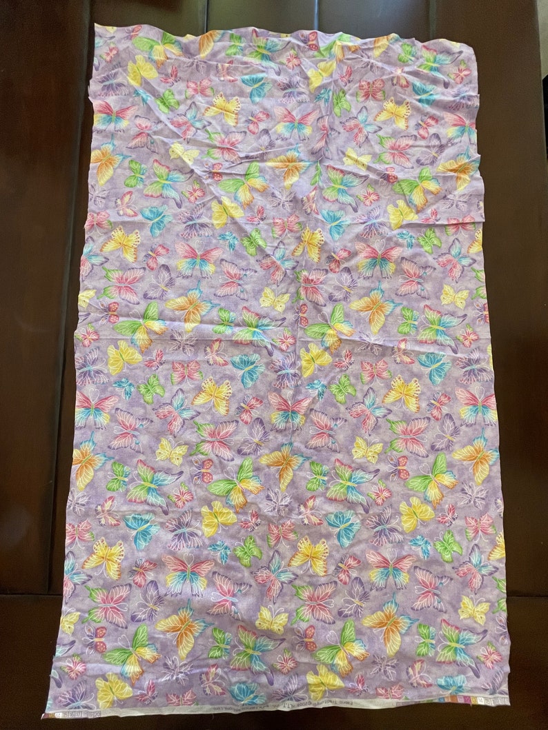May include: Purple fabric with a repeating pattern of colourful butterflies. The butterflies are in various shades of pink, yellow, green, and blue.