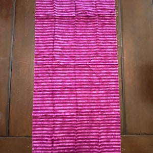 May include: A long piece of fabric with a pink and white striped pattern. The fabric is folded in half and has a white edge.