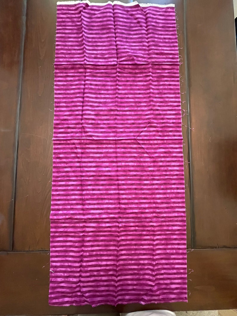 May include: A long piece of fabric with a pink and white striped pattern. The fabric is folded in half and has a white edge.