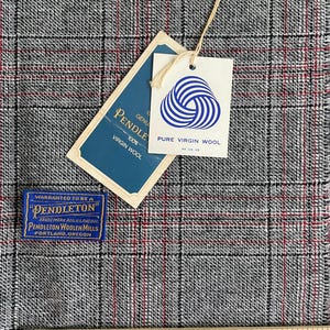 May include: A grey, black, and red plaid fabric with a Pendleton brand tag, a white tag with a blue wool logo reading PURE VIRGIN WOOL, and a blue tag reading WARRANTED TO BE A PENDLETON. A wooden ruler shows a scale in inches at the bottom.