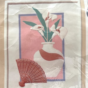 May include: A framed artwork featuring a white vase with calla lilies, a red and white fan, and a pink and blue background. The artwork is in a white frame.