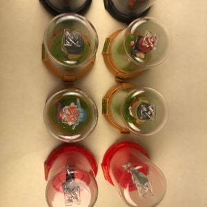 Puede incluir: Ocho peque&ntilde;as figuras de vidrio con c&uacute;pula con diferentes personajes en su interior. Las c&uacute;pulas est&aacute;n sobre una superficie blanca. Los personajes llevan todos sombreros y tienen una Z en el pecho.