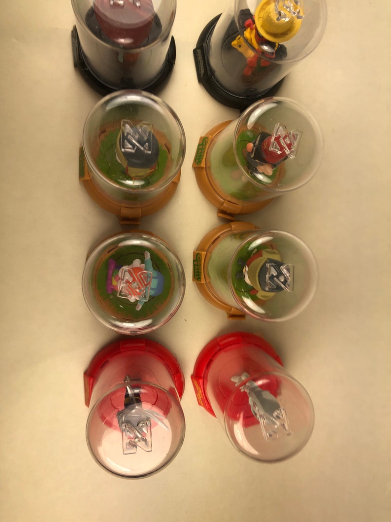 Puede incluir: Ocho peque&ntilde;as figuras de vidrio con c&uacute;pula con diferentes personajes en su interior. Las c&uacute;pulas est&aacute;n sobre una superficie blanca. Los personajes llevan todos sombreros y tienen una Z en el pecho.