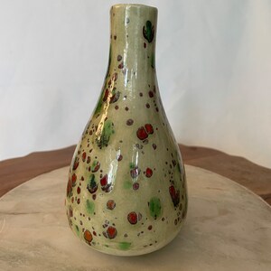 May include: A small, pear-shaped ceramic vase with a green, white, and red speckled glaze.