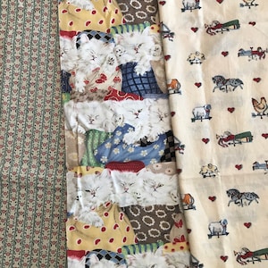 May include: Two fabric swatches, one with a repeating pattern of white kittens sleeping in colorful patchwork bedding, and the other with a repeating pattern of white horses, sheep, and roosters on a cream background.