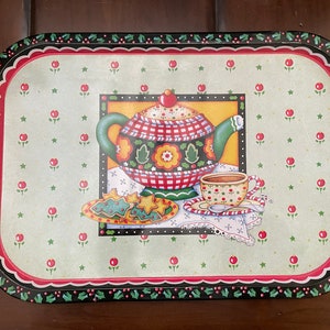 May include: A green and red metal serving tray with a festive holiday design. The tray features a teapot, a cup, and cookies. The design is on a white background with red dots and green stars.