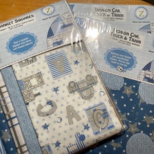 May include: Packages of fabric squares and iron-on appliques for baby blankets. The fabric squares are 10 x 10 inches and feature patterns with letters, stars, and trucks. The iron-on appliques are pre-cut and ready to iron on.