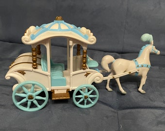 May include: A white and blue toy carriage with a gold trim and a white horse. The carriage has a blue roof and a white interior. The horse has a blue plume on its head.