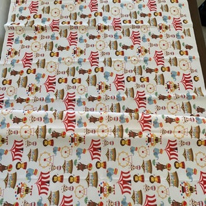 May include: White fabric with a repeating pattern of a circus theme. The pattern includes red and white striped tents, elephants, monkeys, clowns, Ferris wheels, and other circus elements.