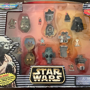 May include: A Star Wars Micro Machines toy set in a clear plastic box. The set includes a variety of characters and vehicles from the Star Wars universe, including Yoda, Darth Vader, and a TIE fighter. The box also includes a trading card.