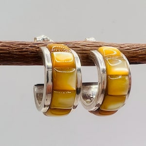 May include: A pair of silver hoop earrings featuring a row of square, polished golden-yellow shell inlays. The earrings have a curved, semi-circular design with a smooth metallic finish, showcasing the natural luster of the yellow shell segments.