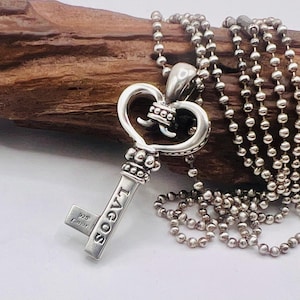 May include: A sterling silver key pendant on a ball chain necklace. The key features an ornate heart-shaped bow with beaded detailing and the word LAGOS engraved on the shaft. The bit of the key is stamped with 925 and Caviar hallmarks.