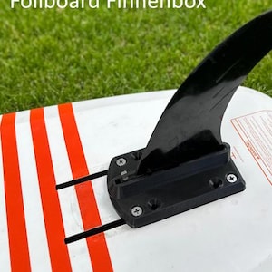 Peut inclure: Une planche de surf à rayures blanches et rouges avec un boîtier de dérives noir et une dérive noire. Le boîtier de dérives a une vis noire sur le dessus et une vis noire sur le dessous. La dérive est fixée au boîtier de dérives avec une vis noire.