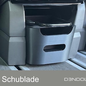 Könnte beinhalten: Eine dunkelgraue Aufbewahrungsschublade, möglicherweise für ein Fahrzeug, mit rechteckiger Öffnung und gebogenem Griff. Der Text "T7 Schublade" ist unten sichtbar, zusammen mit dem D3NDOLAB-Logo.