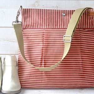 May include: A red and cream striped canvas tote bag with a long beige strap and a small brown leather tag that says "FABRICS 1998".