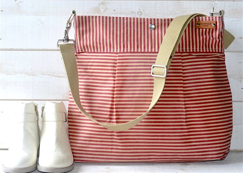 May include: A red and cream striped canvas tote bag with a long beige strap and a small brown leather tag that says "FABRICS 1998".