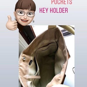May include: A beige tote bag interior featuring five interior pockets of varying sizes and an integrated key holder. The bag has a light-colored fabric lining, a small black brand tag, and two sturdy shoulder straps attached to the top edges.