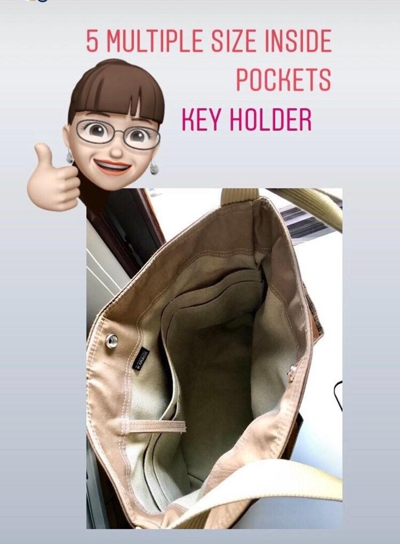 May include: A beige tote bag interior featuring five interior pockets of varying sizes and an integrated key holder. The bag has a light-colored fabric lining, a small black brand tag, and two sturdy shoulder straps attached to the top edges.