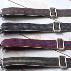 May include: Four different striped fabric straps with silver metal clasps and loops. The straps are in various colors, including red, black, green, and brown.