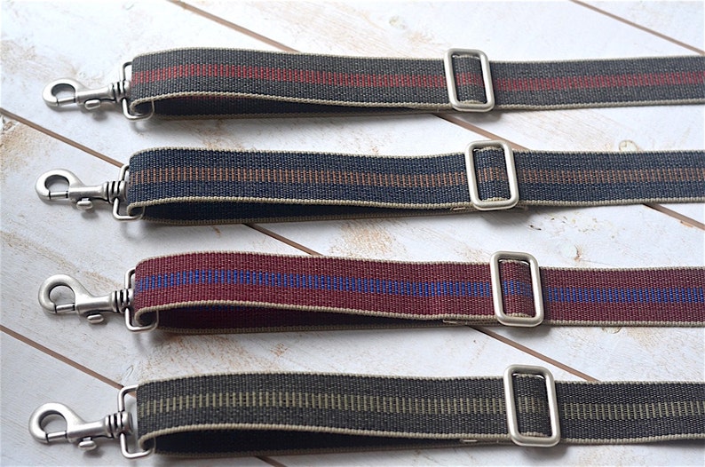 May include: Four different striped fabric straps with silver metal clasps and loops. The straps are in various colors, including red, black, green, and brown.