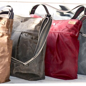 May include: Four vertical tote bags with adjustable shoulder straps, each featuring a pleated front, side pockets, and a small rectangular brand tag. The bags are rendered in tan, dark brown, deep red, and slate gray, all with a waxed finish.