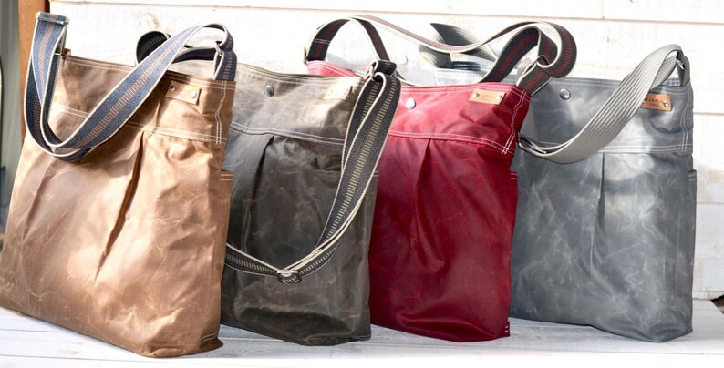 May include: Four vertical tote bags with adjustable shoulder straps, each featuring a pleated front, side pockets, and a small rectangular brand tag. The bags are rendered in tan, dark brown, deep red, and slate gray, all with a waxed finish.