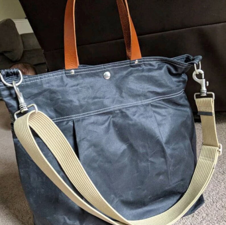 May include: A dark blue canvas tote bag with brown leather handles and a beige adjustable shoulder strap. The bag has a zipper closure and a silver metal clasp.