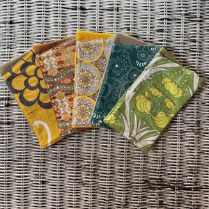 May include: A collection of five fabric items with various patterns and colors. The items include a yellow floral design, a geometric pattern with red and brown accents, a yellow and white circular design, a teal and white design, and a green floral pattern.
