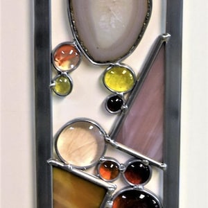 May include: A stained glass window panel with a geometric design featuring circles, triangles, and squares in shades of yellow, orange, brown, pink, and white.