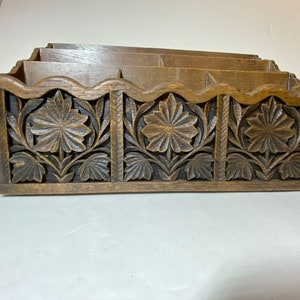 Peut inclure: Organisateur de bureau en bois avec un motif floral sculpté. Il comporte plusieurs compartiments pour ranger papiers et documents. La façade présente un relief détaillé de fleurs et de feuilles, ajoutant une touche décorative.