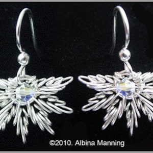 May include: A pair of silver-toned wire earrings. Each earring features a starburst design with a central iridescent crystal. The earrings have a hook closure. The background is black.