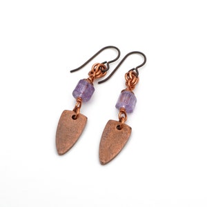 May include: A pair of copper earrings with a purple glass bead and a copper teardrop shape.