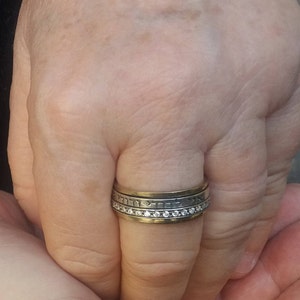 K&ouml;nnte beinhalten: Ein Silber- und Goldring mit einer Reihe kleiner Diamanten und hebr&auml;ischer Schrift.