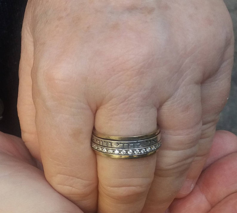 K&ouml;nnte beinhalten: Ein Silber- und Goldring mit einer Reihe kleiner Diamanten und hebr&auml;ischer Schrift.