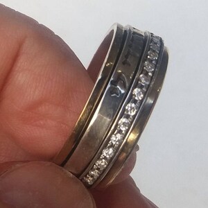 K&ouml;nnte beinhalten: Ein drehbarer Ring aus Silber und Gold mit einer Reihe von klaren Zirkonia-Steinen. Der Ring ist mit hebr&auml;ischer Schrift graviert.