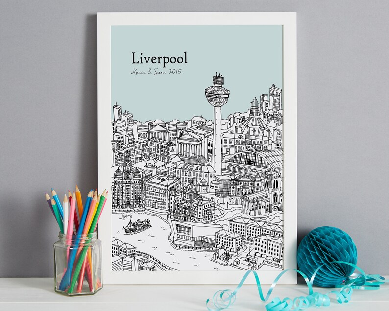 Op de afbeelding: Een zwart-witte lijntekening van de skyline van Liverpool, inclusief het Liver Building, het Royal Liver Building en de Radio City Tower. De tekening is op een lichtblauwe achtergrond met de tekst "Liverpool" en "Katie & Sam 2015" in zwart.