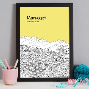 May include: A black framed print with a yellow background and a black and white illustration of the city of Marrakech, Morocco. The text "Marrakech" and "Summer 2016" is printed in black at the top of the print.