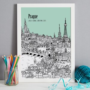 Op de afbeelding: Een zwart-witte lijntekening van de skyline van Praag met de tekst "Praag" en "Jack & Sarah, Kerstmis 2015" op een lichtblauwe achtergrond.