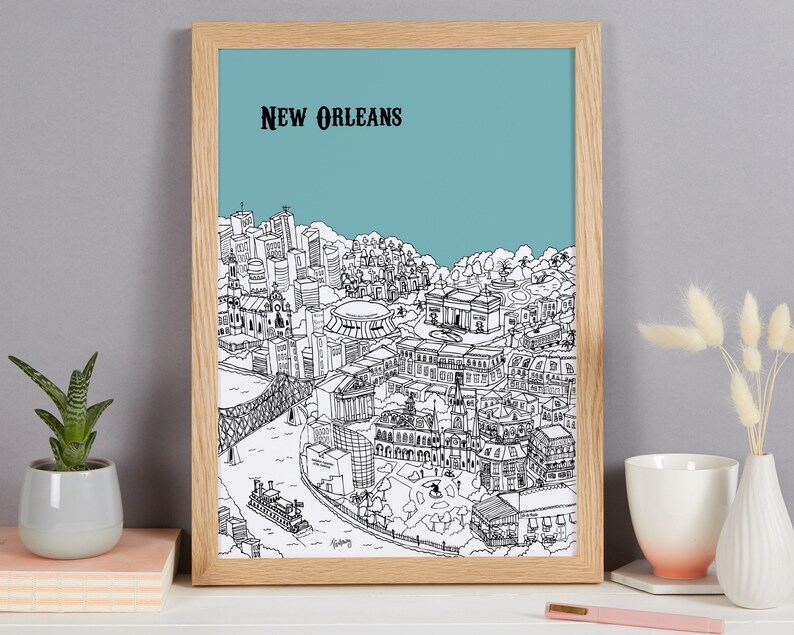 May include: A framed black and white line drawing of the New Orleans skyline against a light blue background. The drawing includes iconic buildings and landmarks, such as the French Quarter, the Superdome, and the Mississippi River.
