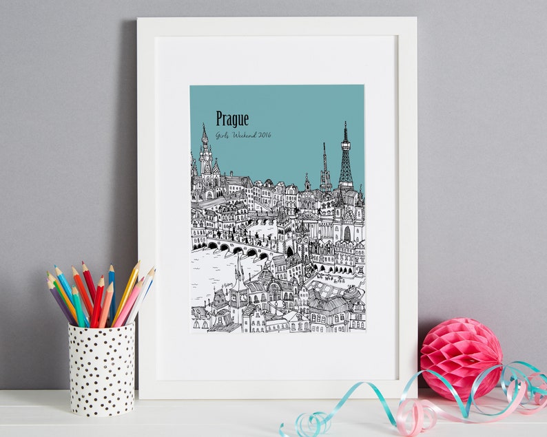 Op de afbeelding: Een zwart-witte illustratie van de skyline van Praag met de tekst "Prague Girls Weekend 2016" op een teal achtergrond. De illustratie is ingelijst in een wit frame.