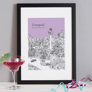 Op de afbeelding: Een zwart ingelijst print met een paarse achtergrond met een lijntekening van de skyline van Liverpool. De tekst "Liverpool" staat bovenaan de print, met de tekst "Jude, Sam & Wendy - 2014" eronder.