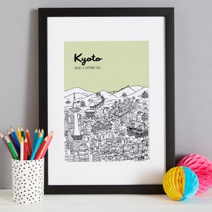 May include: A black framed print with a green background and a black and white illustration of the city of Kyoto, Japan. The text "Kyoto" is written in black cursive lettering at the top of the print. The text "August & September 2016" is written in black lettering below the word "Kyoto".