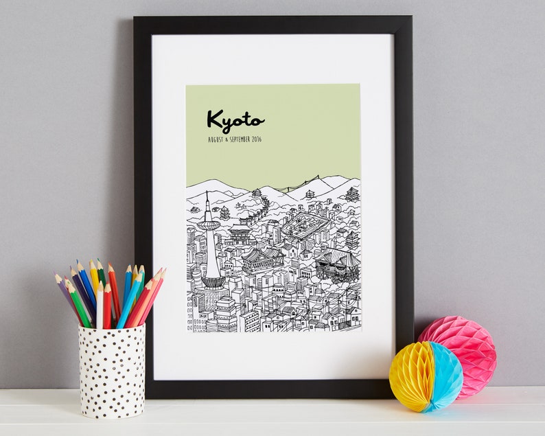 May include: A black framed print with a green background and a black and white illustration of the city of Kyoto, Japan. The text "Kyoto" is written in black cursive lettering at the top of the print. The text "August & September 2016" is written in black lettering below the word "Kyoto".
