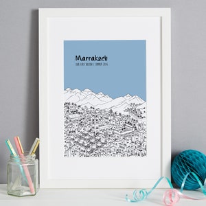 May include: A black and white line drawing of the city of Marrakech, Morocco, with the text "Marrakech Our First Holiday - Summer 2016" above the drawing. The drawing is on a light blue background and is framed in a white frame.