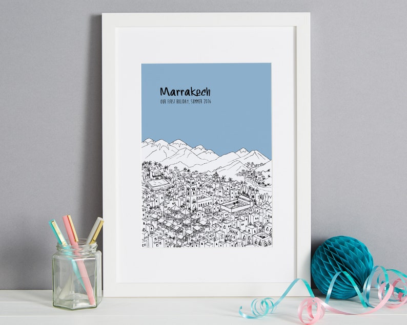 May include: A black and white line drawing of the city of Marrakech, Morocco, with the text "Marrakech Our First Holiday - Summer 2016" above the drawing. The drawing is on a light blue background and is framed in a white frame.