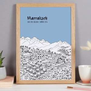 May include: A framed print with a black and white illustration of the city of Marrakech, Morocco. The print has a light blue background and the text "Marrakech" and "Our first holiday, Summer 2016" at the top.