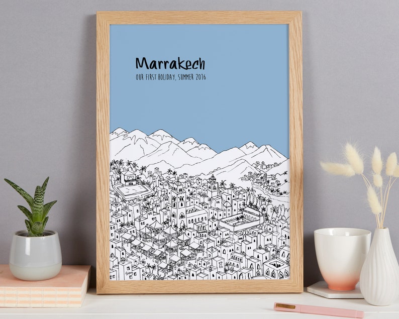 May include: A framed print with a black and white illustration of the city of Marrakech, Morocco. The print has a light blue background and the text "Marrakech" and "Our first holiday, Summer 2016" at the top.