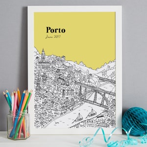 May include: A framed black and white illustration of Porto, Portugal, with a yellow background. The artwork depicts the city's architecture, a bridge, and the text "Porto June 2017". Colored pencils in a glass jar and a blue paper decoration are in the foreground.