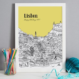 May include: A black and white line drawing of the city of Lisbon, Portugal, on a yellow background. The drawing includes buildings, streets, and landmarks. The text "Lisbon" and "Happy Holidays 2017" is printed in black at the top of the image.